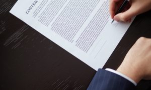 Image of businessman hand with pen signing contract at workplace